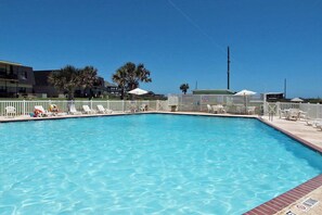 A rectangular swimming pool with a white fence and lounge chairs around it. - Island Oasis- Beach Access Pools Volleyball (Port Aransas)