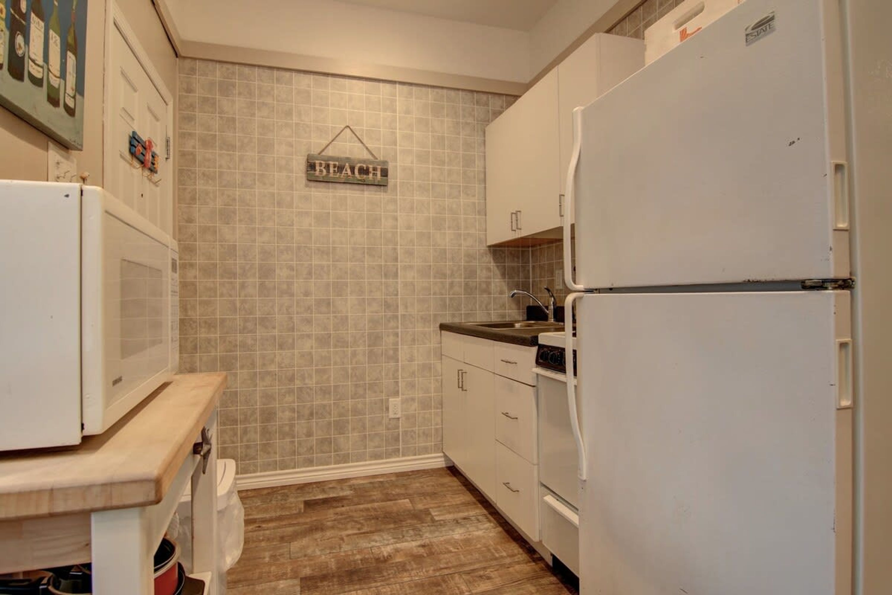Una cocina compacta con electrodomésticos blancos, encimera de madera y salpicadero de azulejos.