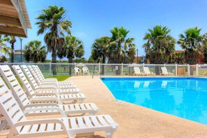 A poolside area with white lounge chairs, a clear blue pool, and palm trees in the background. - Island Oasis- Beach Access Pools Volleyball (Port Aransas)