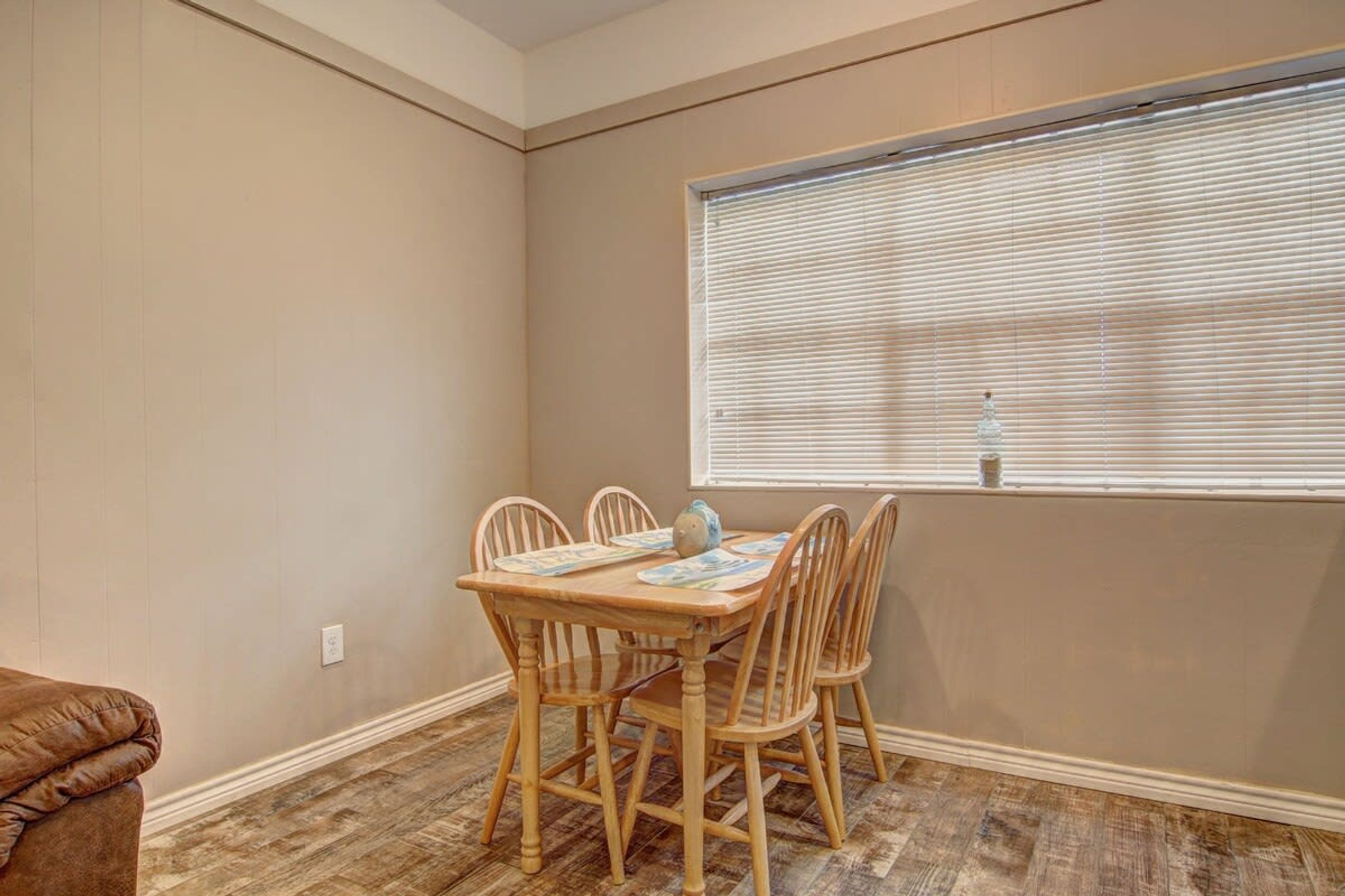 Un comedor con una mesa y sillas de madera, una ventana con persianas, y un sofá de cuero marrón.