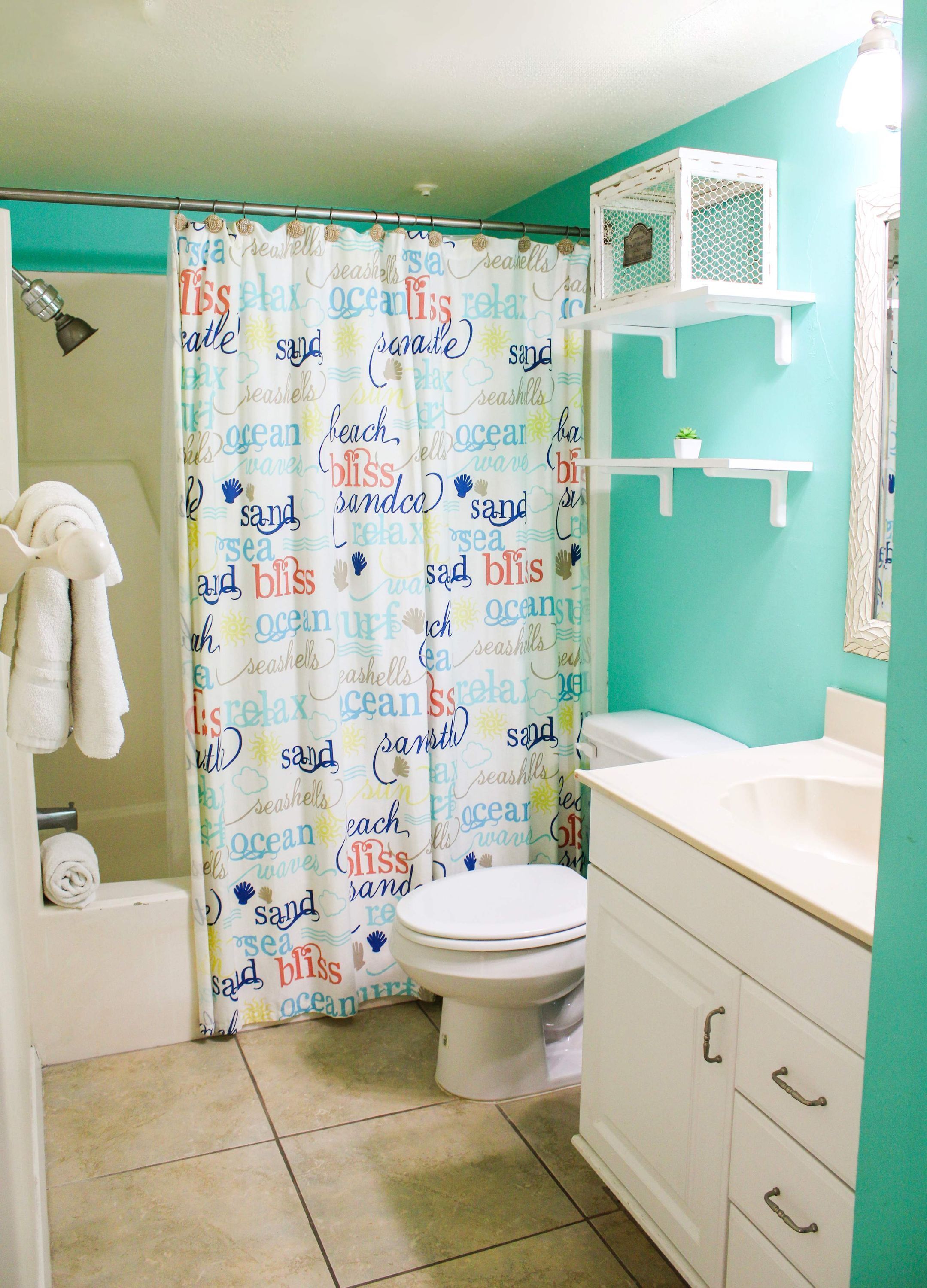 A bathroom with a shower curtain featuring ocean-related words, a toilet, a sink, and a towel rack.