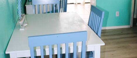 Un comedor con una mesa blanca y sillas azules, un reloj de pared y un cartel de bienvenida.