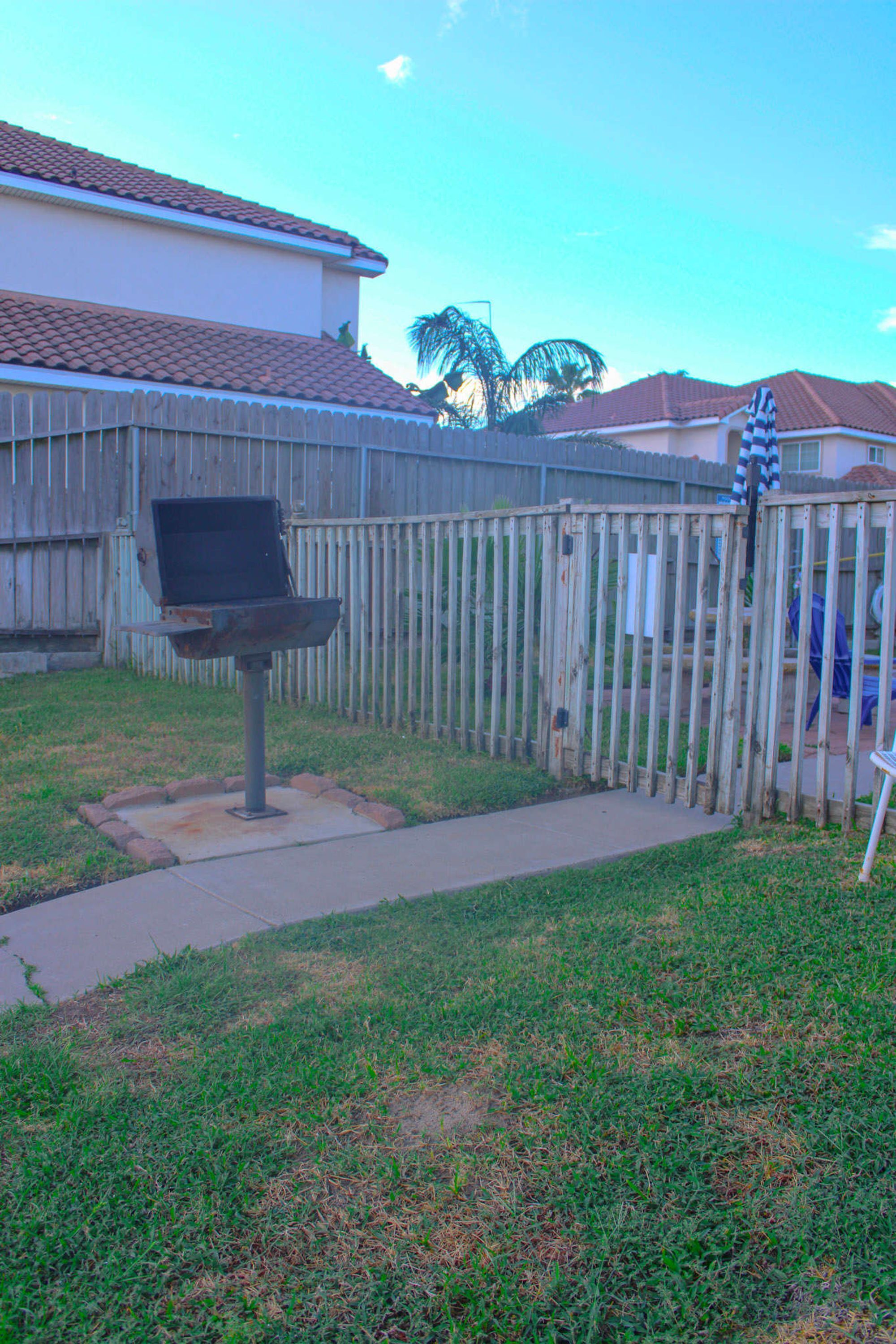 A backyard with a barbecue grill, a wooden fence, and a house in the background.