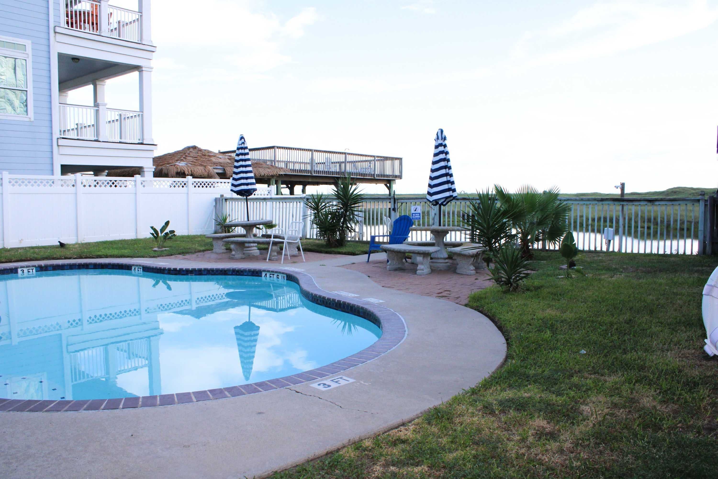 Zwembad met bakstenen rand, omringd door een gazon en een witte hek.