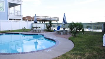 Une piscine bordée de briques, entourée d’une pelouse et d’une clôture blanche.
