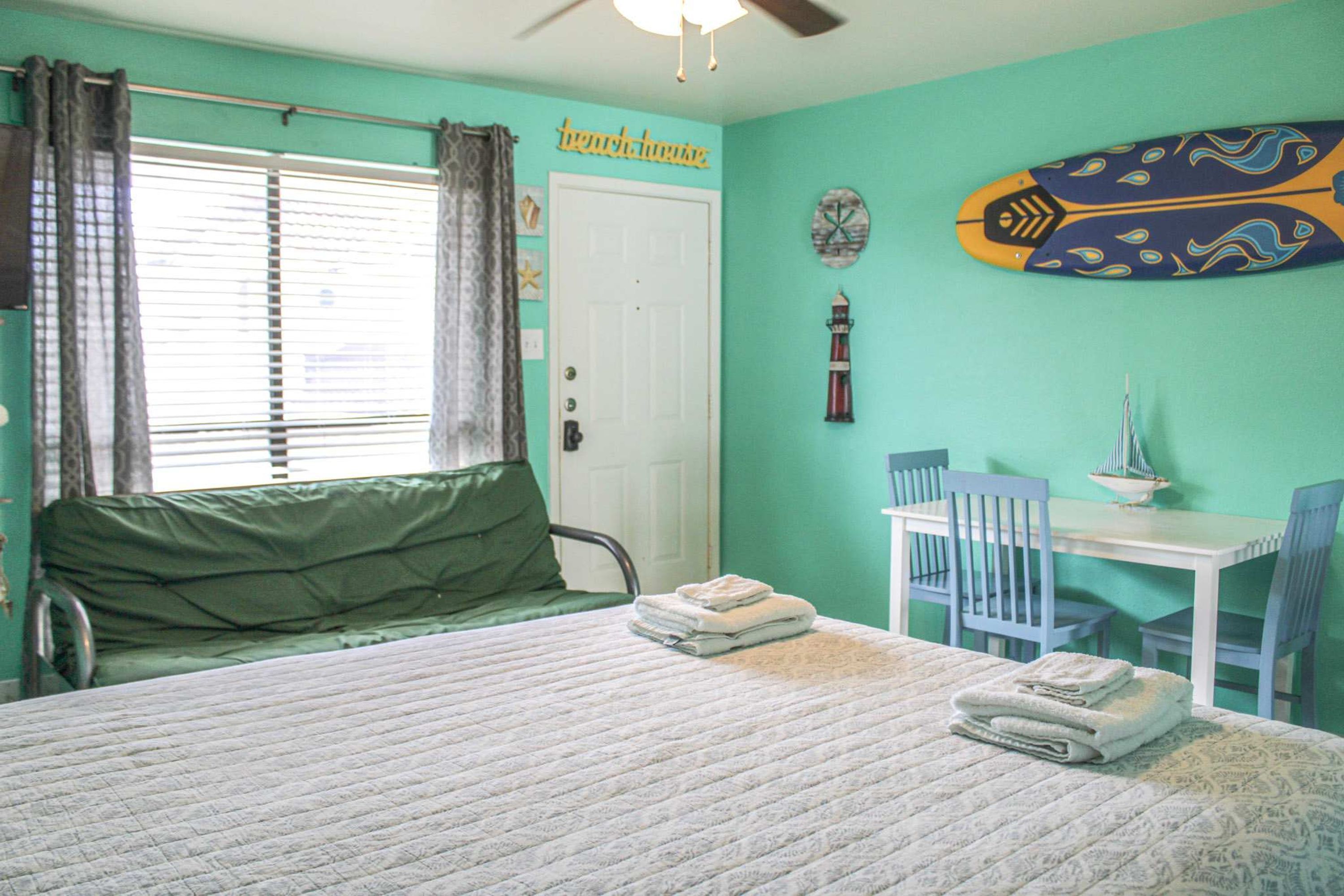 Une chambre à coucher avec un lit, un bureau et une chaise. Il y a une fenêtre avec des rideaux, une porte et une horloge murale.