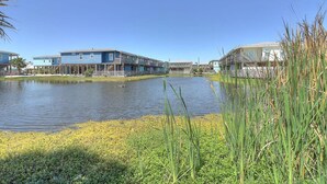 A waterfront property with a large body of water, a grassy area, and buildings with balconies. - Stairway to Seven- Private Pool Hammocks (Port Aransas)