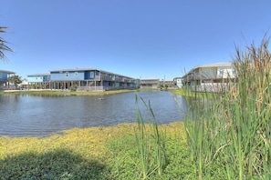 A waterfront property with a large body of water, a grassy area, and buildings with balconies. - Stairway to Seven- Private Pool Hammocks (Port Aransas)