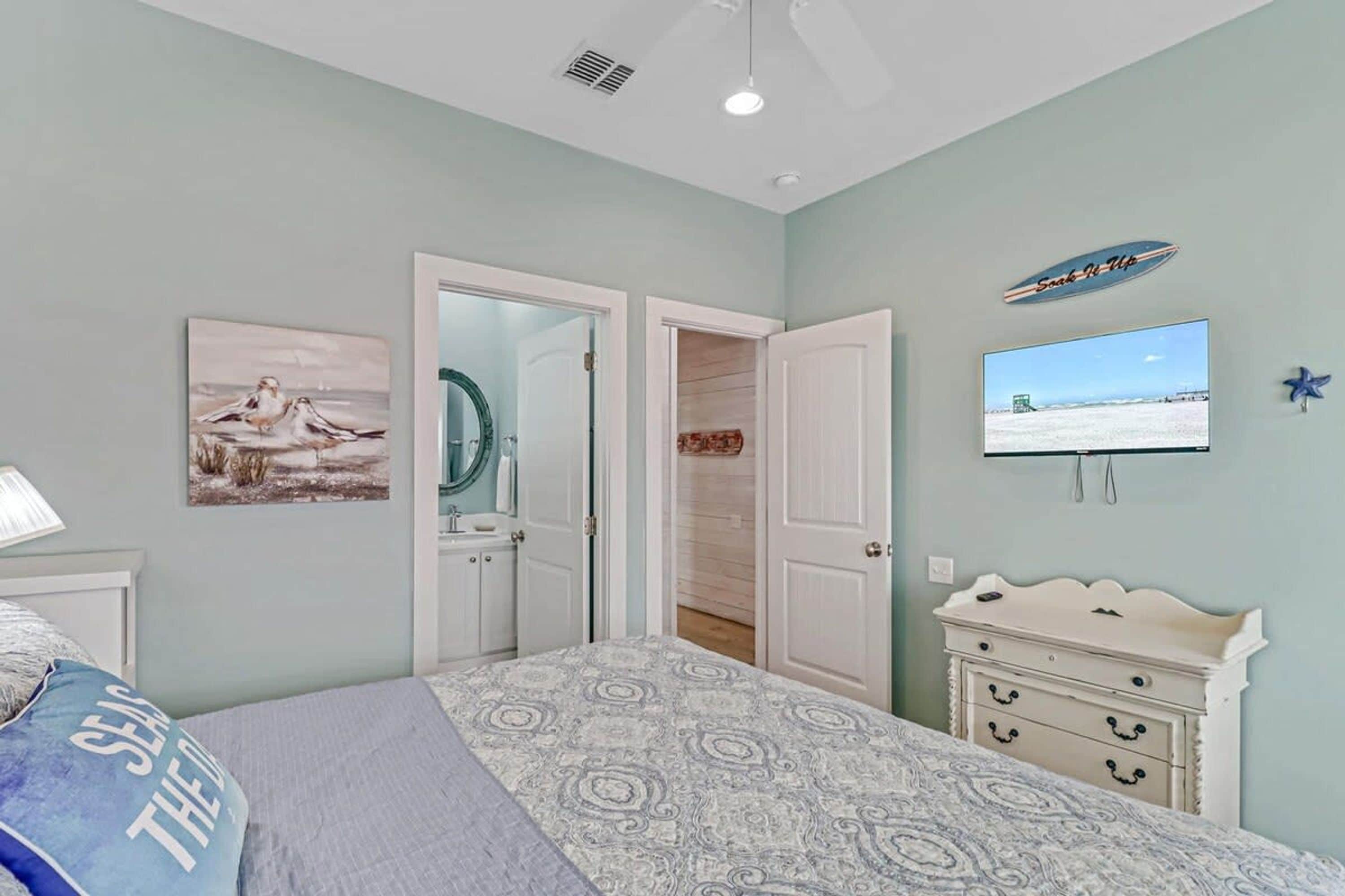 A bedroom with a bed, a dresser, a television, and a door leading to another room.