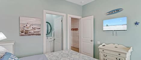 A bedroom with a bed, a dresser, a television, and a door leading to another room.