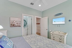 A bedroom with a bed, a dresser, a television, and a door leading to another room. - Stairway to Seven- Private Pool Hammocks (Port Aransas)