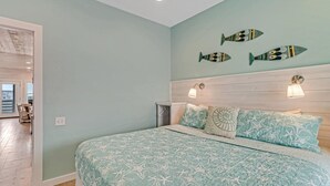 A bedroom with a bed, two wall-mounted lights, and three fish wall art pieces. - Stairway to Seven- Private Pool Hammocks (Port Aransas)