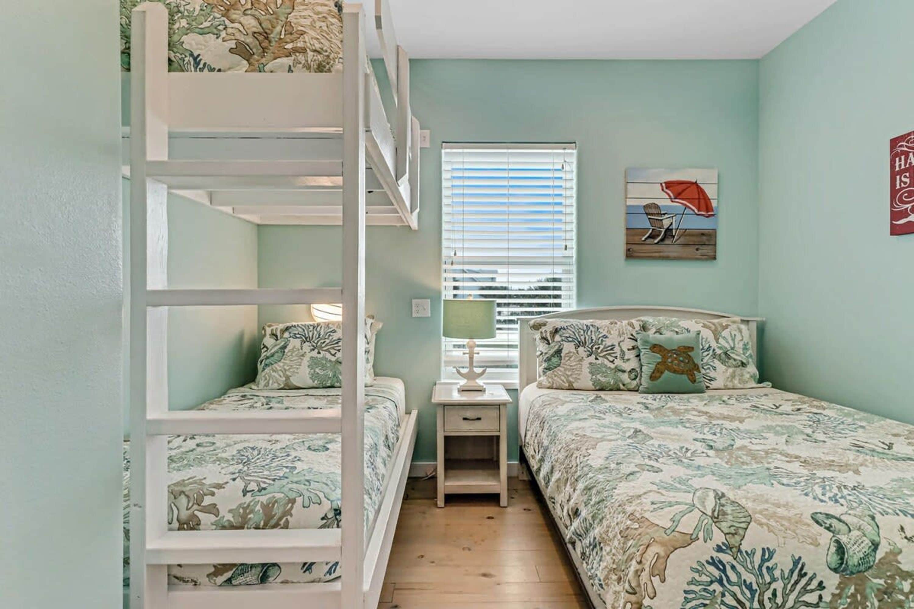 A room with bunk beds, a nightstand, a lamp, and a window with blinds.
