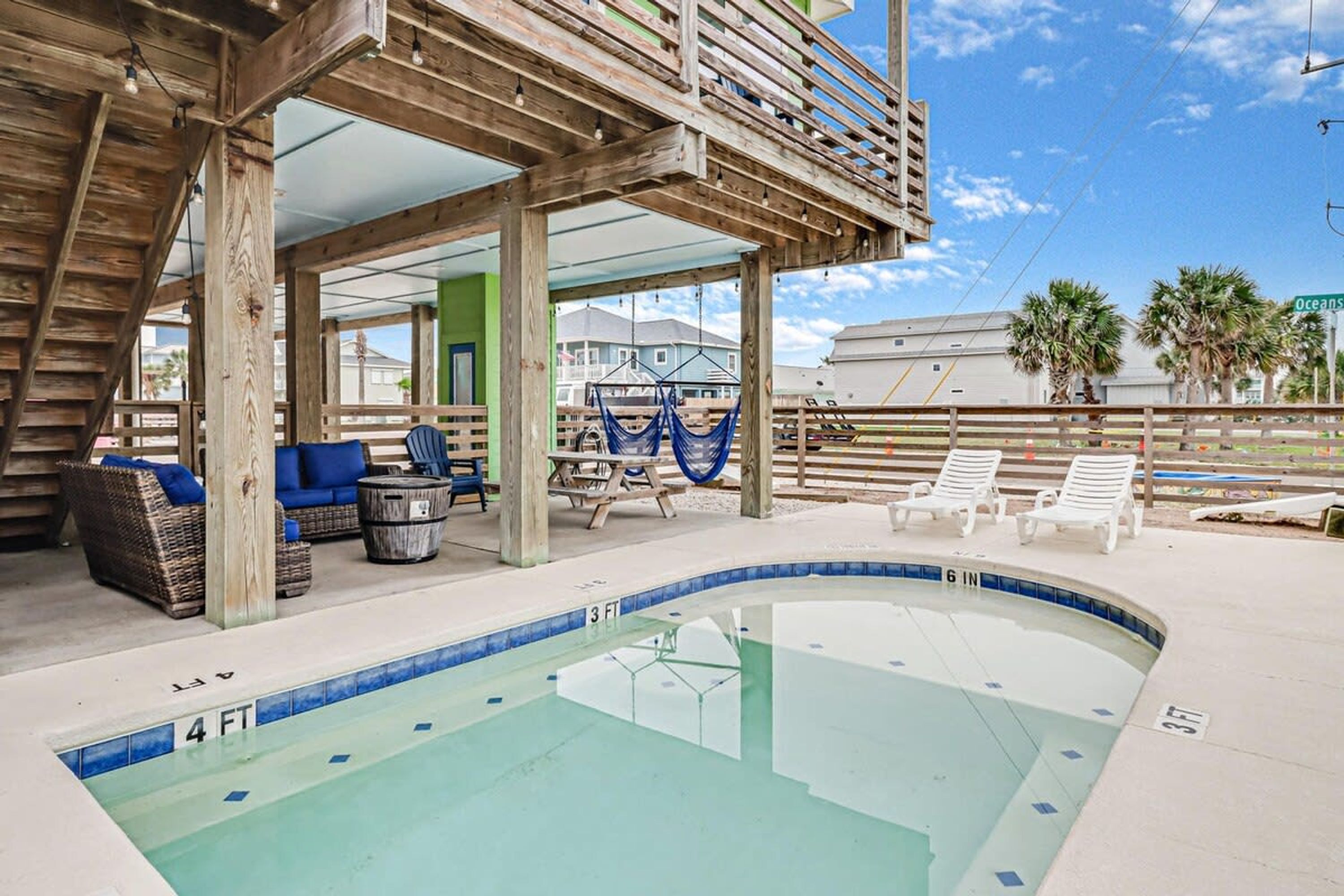 A pool area with a wooden deck, lounge chairs, and a hammock.