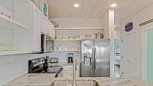 A modern kitchen with a stainless steel refrigerator, a built-in oven, and a sink. - Stairway to Seven- Private Pool Hammocks (Port Aransas)