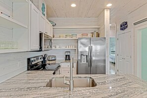 A modern kitchen with a stainless steel refrigerator, a built-in oven, and a sink. - Stairway to Seven- Private Pool Hammocks (Port Aransas)