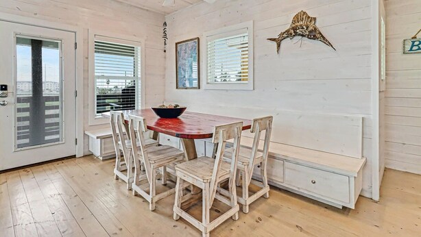 A dining area with a wooden table, white chairs, and a ceiling fan. - Stairway to Seven- Private Pool Hammocks (Port Aransas)