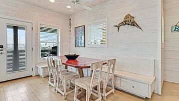 Un coin repas avec une table en bois, des chaises blanches et un ventilateur de plafond.