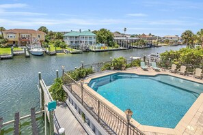 A swimming pool with a deck, a dock with boats, and a marina with houses in the background. - Waterfront Home Pool Golf Cart Dock Sleeps 16 (Destin)