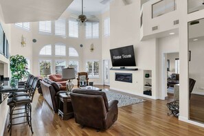 A spacious living room with a high ceiling, large windows, a flat-screen TV, and a fireplace. - Waterfront Home Pool Golf Cart Dock Sleeps 16 (Destin)