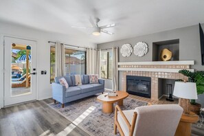 A living room with a sofa, a round coffee table, a fireplace, and a ceiling fan. - Peoria Paradise Basketball Heated Pool Games (Peoria)