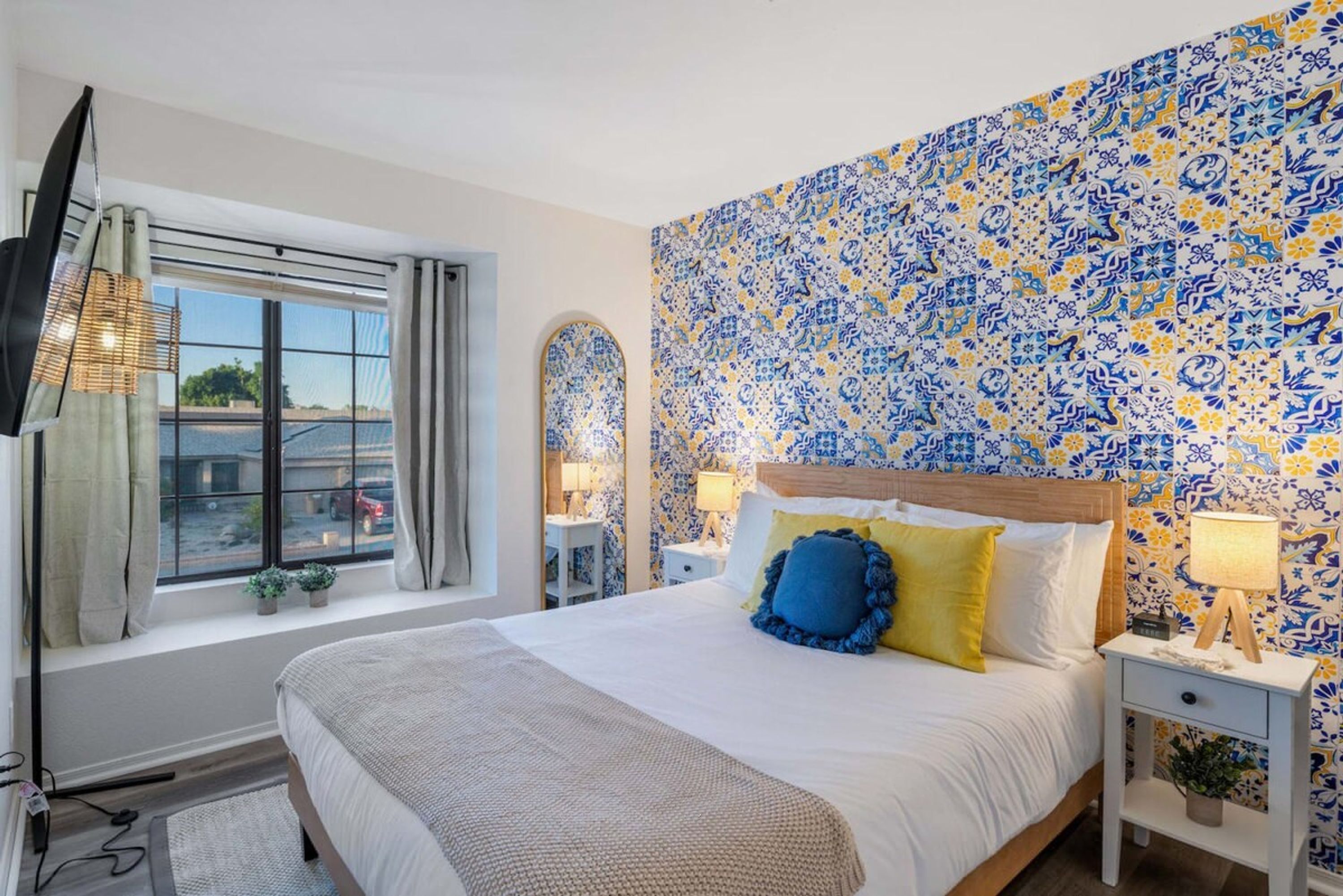 A hotel room with a large bed, a TV, a window with curtains, and a patterned wall.