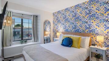 A hotel room with a large bed, a TV, a window with curtains, and a patterned wall.