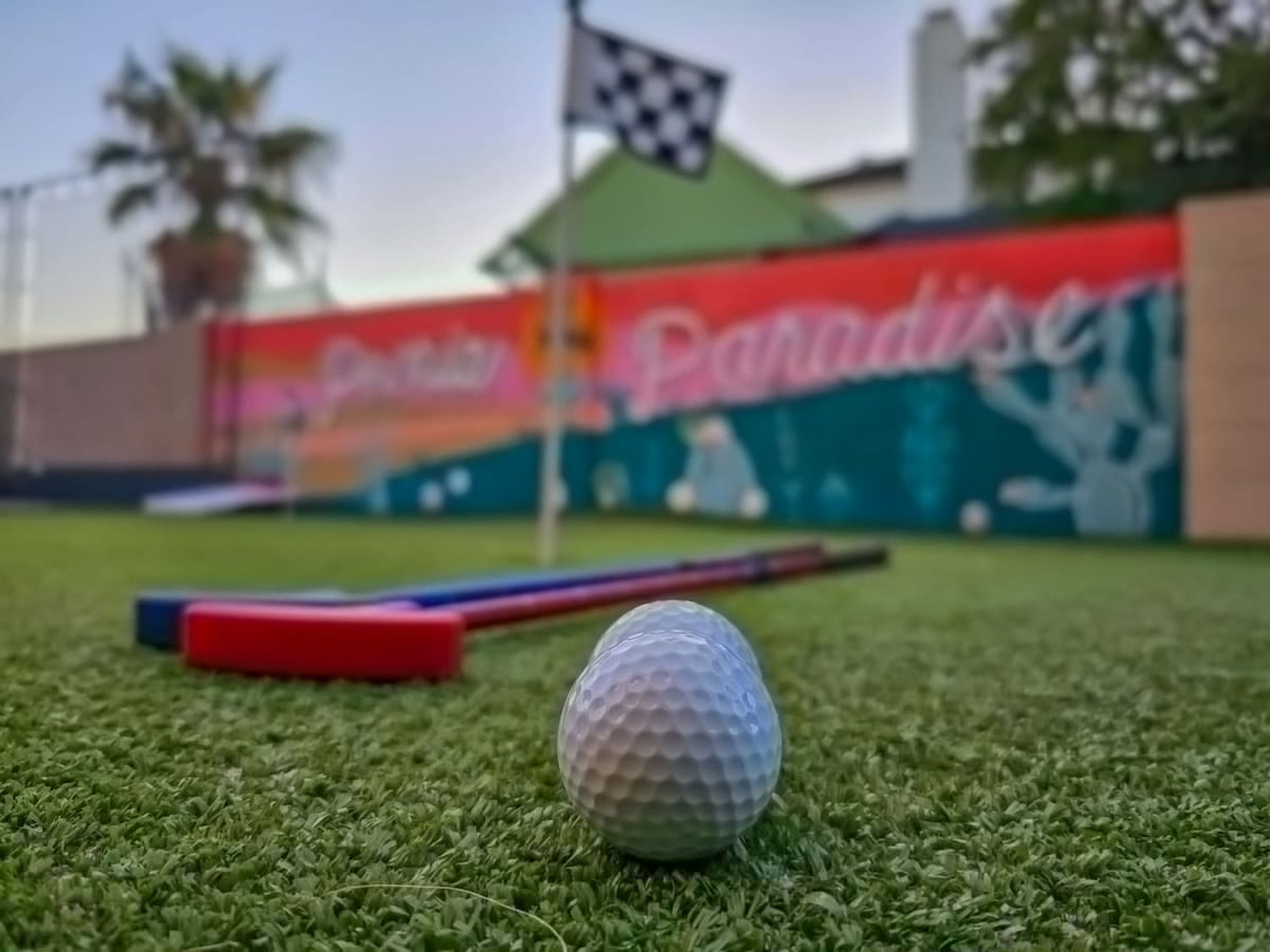 En golfboll på ett konstgräsunderlag, med en rutig flagga och en banderoll i bakgrunden.