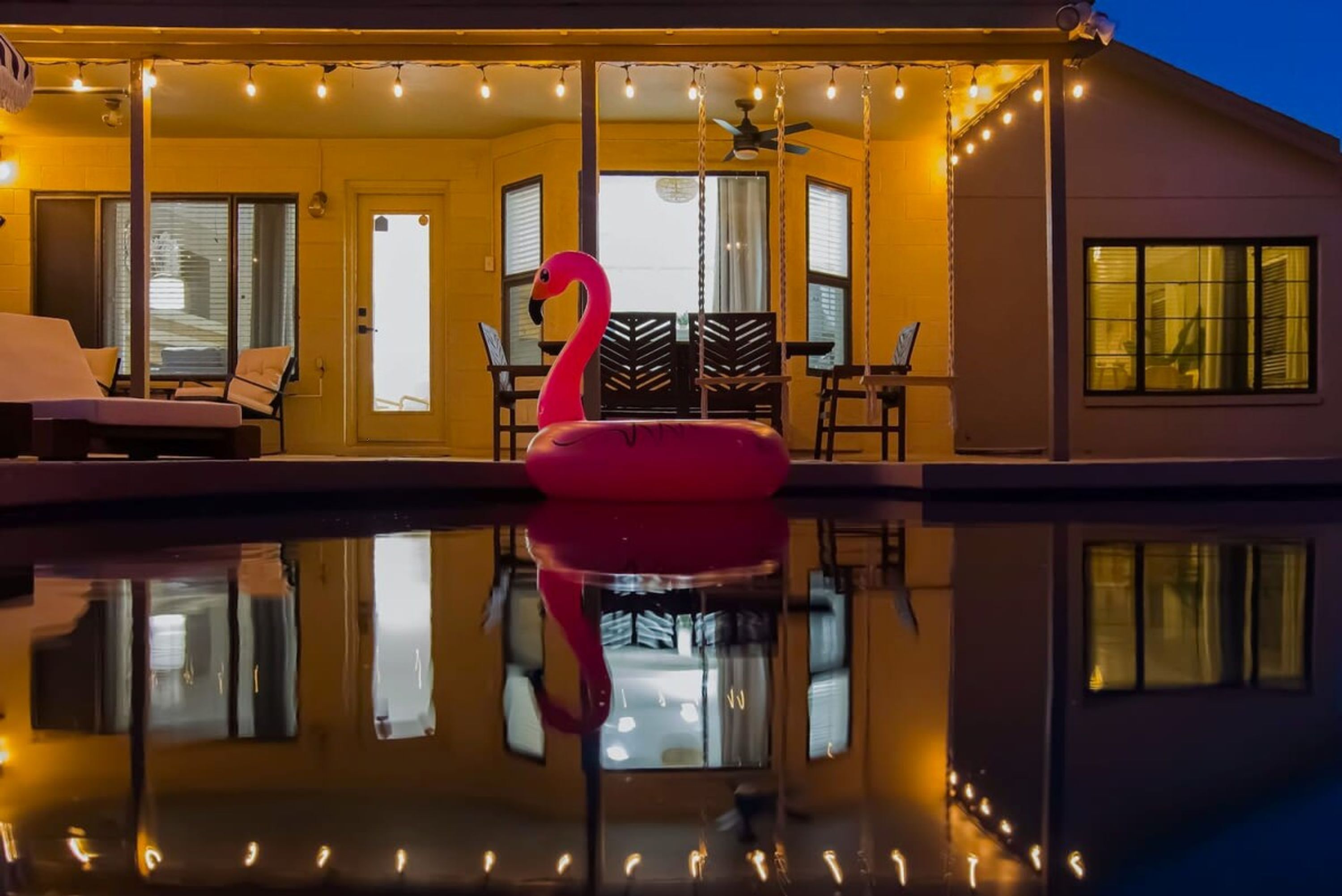 A swimming pool with a flamingo float, surrounded by a covered patio with string lights.