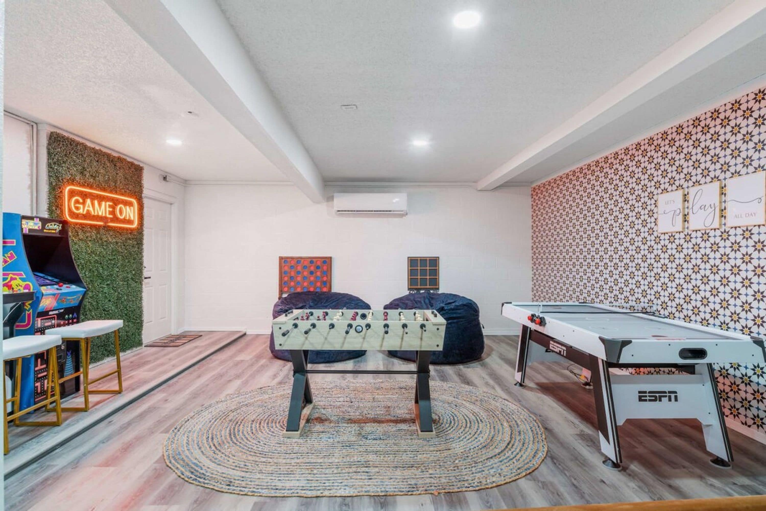 Una habitación con mesa de fútbol, mesa de billar y un letrero de neón que dice 'GAME ON'.