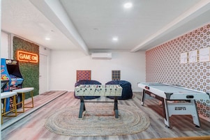 A room with a foosball table, a pool table, and a neon sign reading 'GAME ON'.