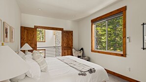 Un dormitorio con una cama grande, una ventana con vistas a árboles y un cabecero de madera.