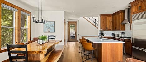 A modern kitchen with wooden cabinets, a large island, and a dining area with a wooden table and chairs.