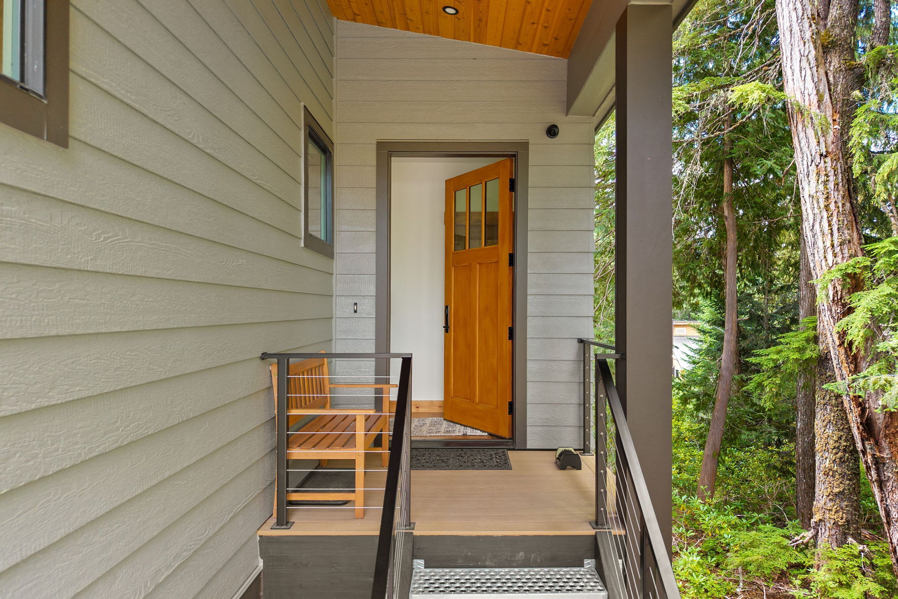 A wooden exterior door leading to a porch with a metal railing and a bench.