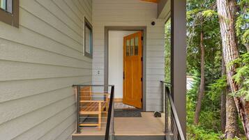 A wooden exterior door leading to a porch with a metal railing and a bench.
