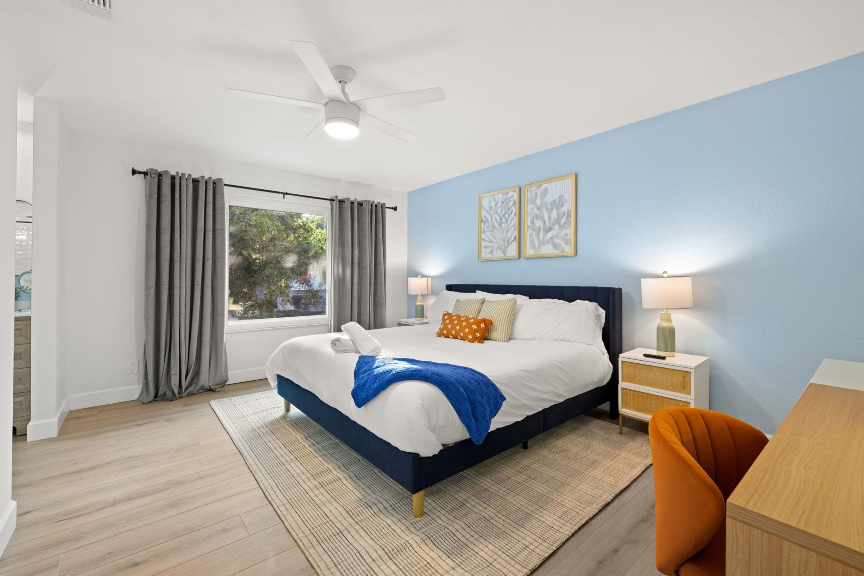 Habitación de hotel con cama, escritorio, silla, mesita de noche, lámpara y ventilador de techo.