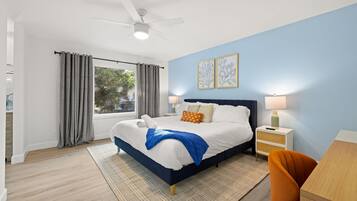 Habitación de hotel con cama, escritorio, silla, mesita de noche, lámpara y ventilador de techo.