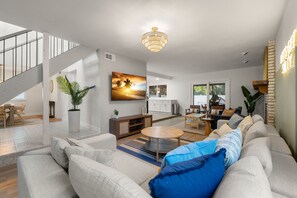 Uma sala de estar ampla com design moderno, apresentando um sofá grande, uma mesa de jantar e uma escada que leva a um andar superior.