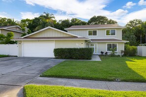 A two-story residential house with a garage, a well-maintained lawn, and a clear sky. - Hot Tub Sportscourt Game Room 5 min to Beach (Seminole)