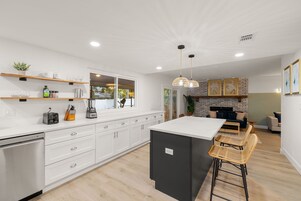 Una cocina moderna con armarios blancos, una isla central y una zona de comedor con taburetes de bar.