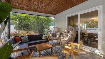 Un patio iluminado por el sol, con techo de madera, un sofá, dos sillones de mimbre, una mesa de comedor y vistas a zonas verdes.