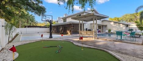 A residential property with a backyard featuring a putting green, a pool, and a covered patio area.