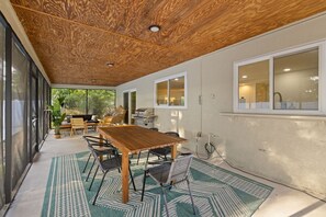 An outdoor dining area with a wooden table and chairs, surrounded by large windows and a ceiling with a wood-like texture. - Hot Tub Sportscourt Game Room 5 min to Beach (Seminole)