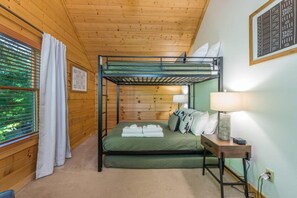 Habitación con literas, un colchón verde, una mesita de noche con lámpara y una ventana con persianas.
