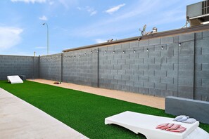 Ein Garten mit Kunstgrasanlage, einem weißen Liegestuhl und einer Betonterrasse.