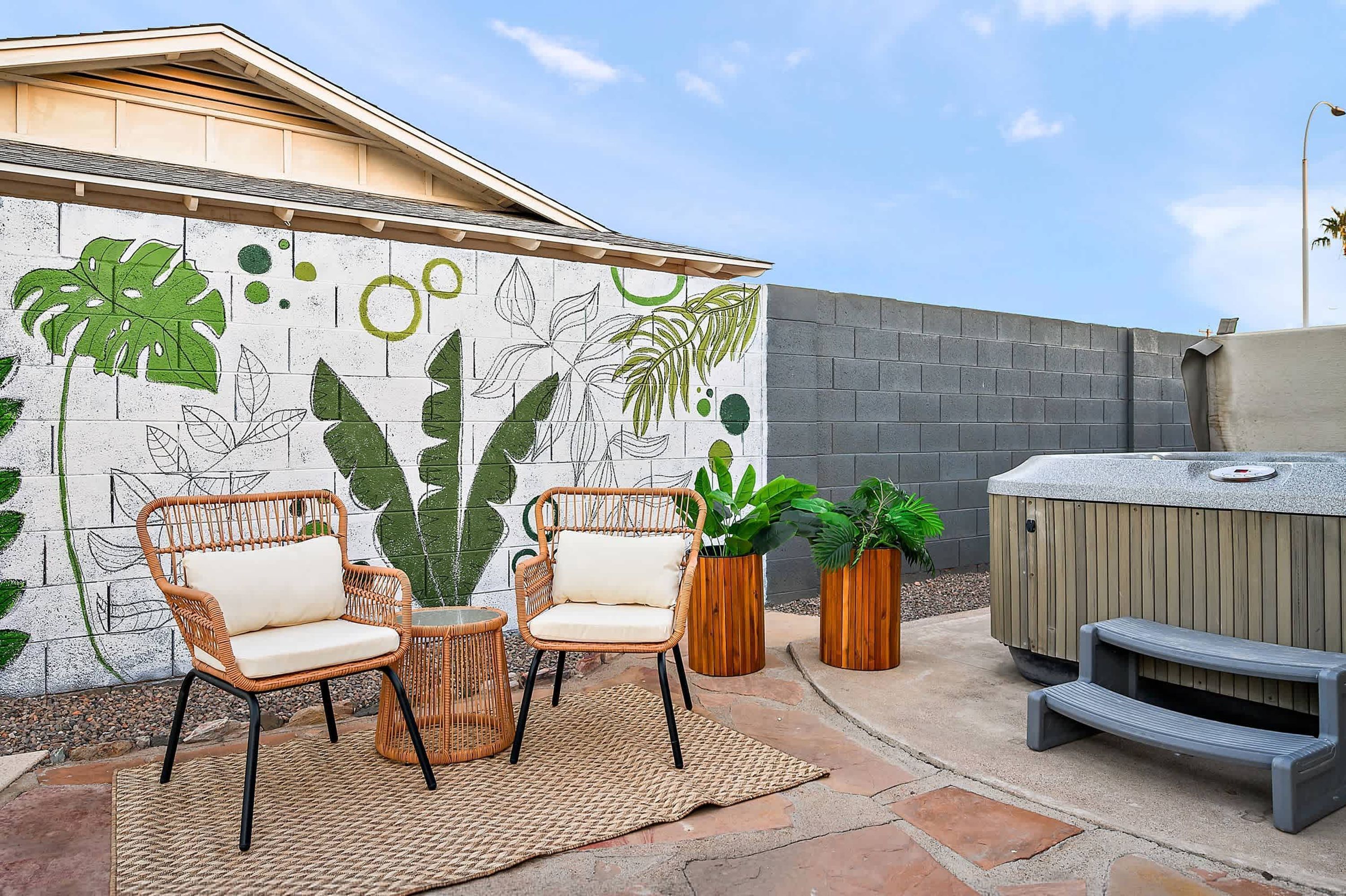 Eine Terrassenfläche mit zwei Korbstühlen, einem Webteppich und einer Wand mit einem botanischen Wandbild.