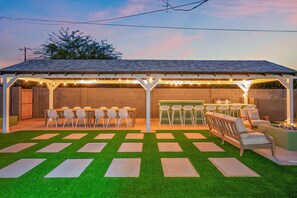 A covered outdoor patio with a dining area, bar, and seating. - The Desert Emerald Pool Hot Tub Games More (Scottsdale)