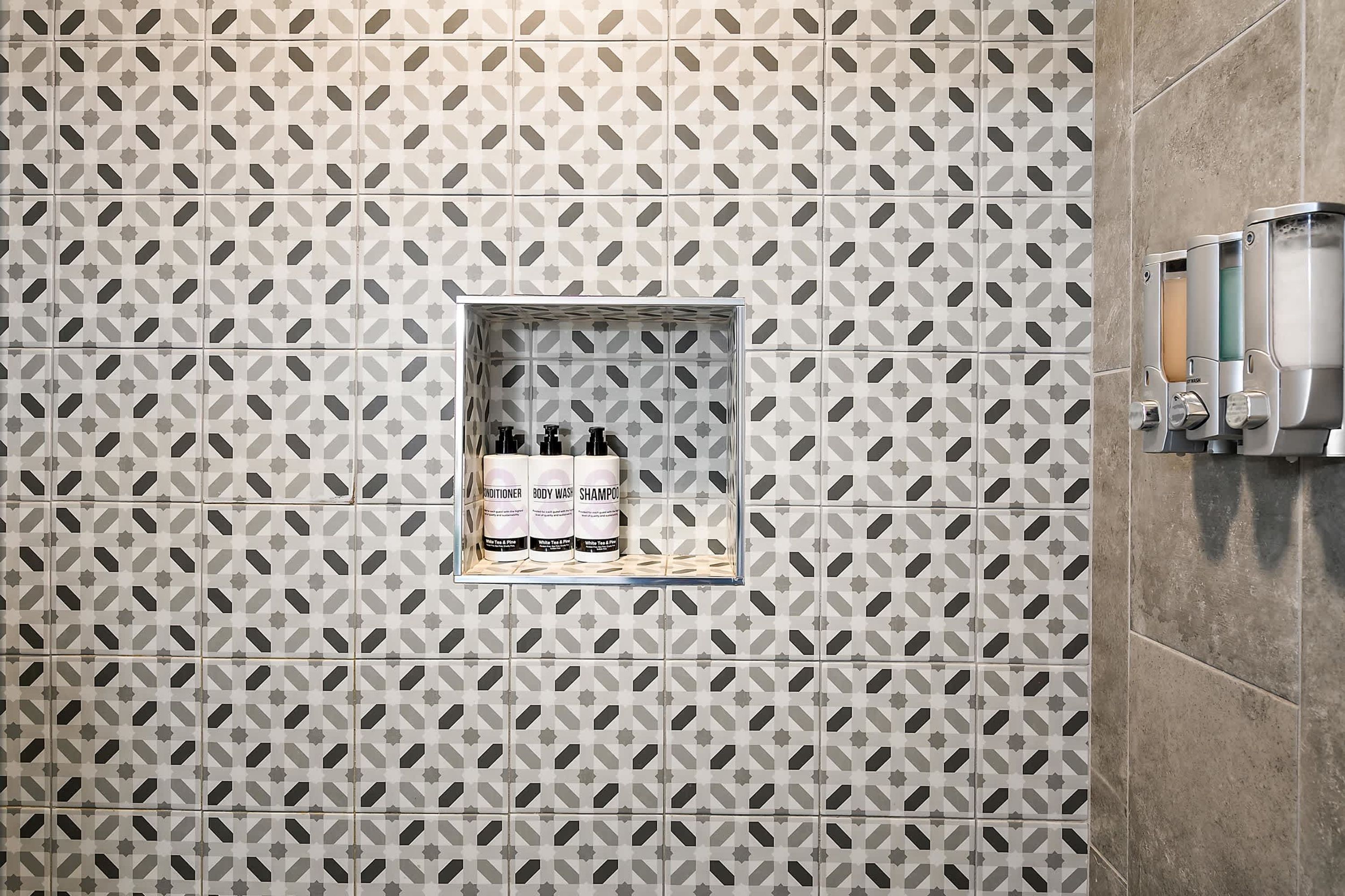 Et badeværelse med en væg i et mønstret flisemønster, en indbygget hylde med toiletartikler og en håndtørrer.