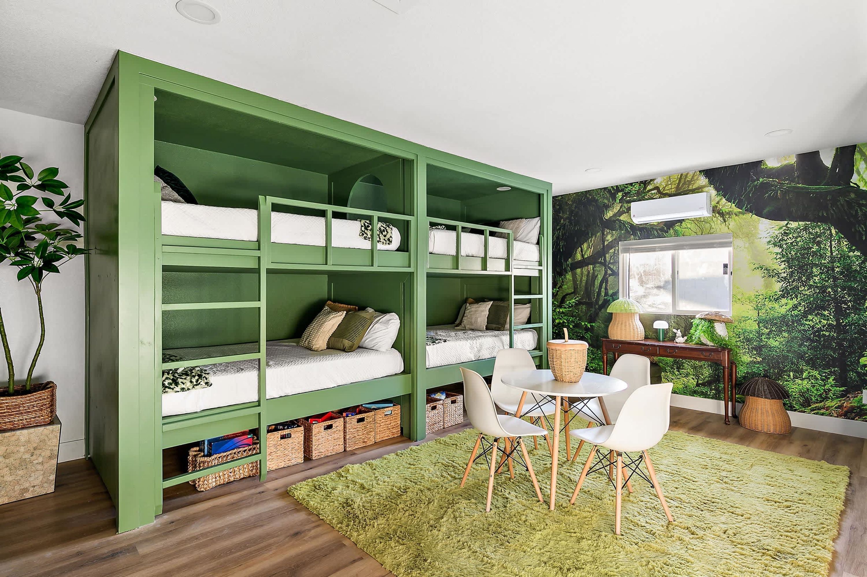 Une chambre avec un lit superposé vert, une petite table avec des chaises, un tapis vert et une fresque murale.
