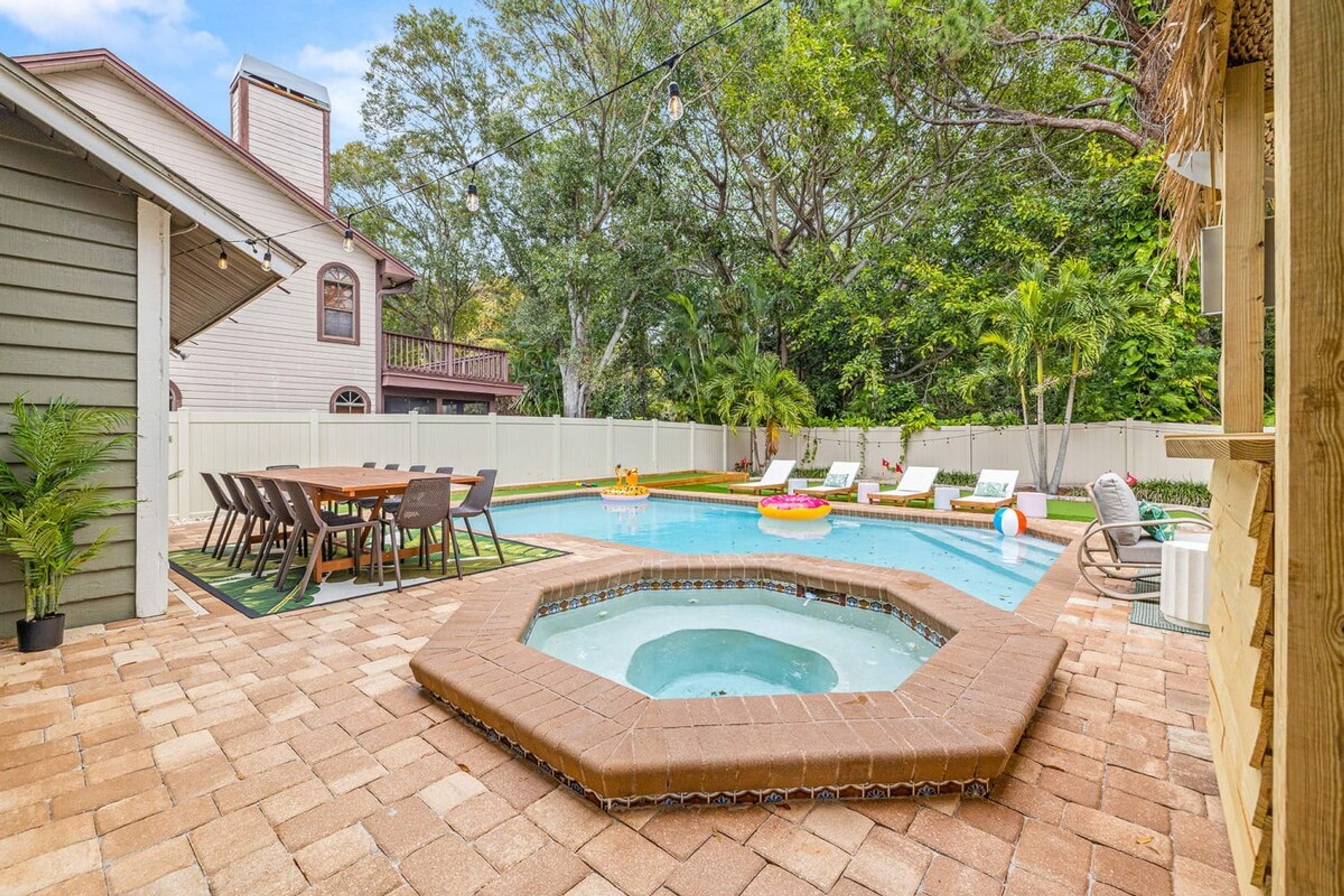 Un patio trasero con piscina, jacuzzi y un comedor con sillas y mesa.